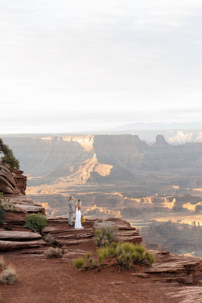 Couple holding hands cliffside, posing for Utah elopement photographer in Moab, Forever Framed by Rachel