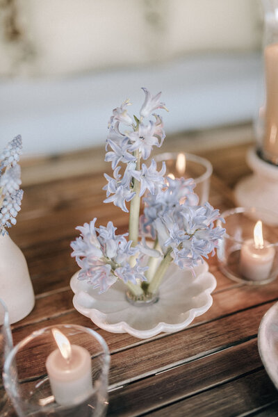 Blue hyacinth ikebana arrangement in a scalloped white trinket dish, sitting beside a small bud vase with blue muscari
