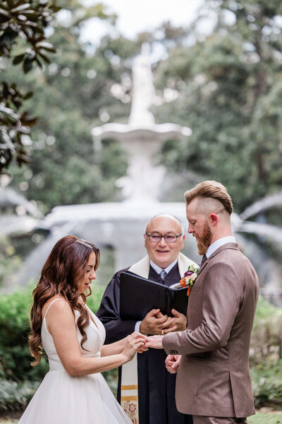 Bride and groom walking hand-in-hand along a brick sidewalk in Savannah, GA, surrounded by historic charm and greenery.