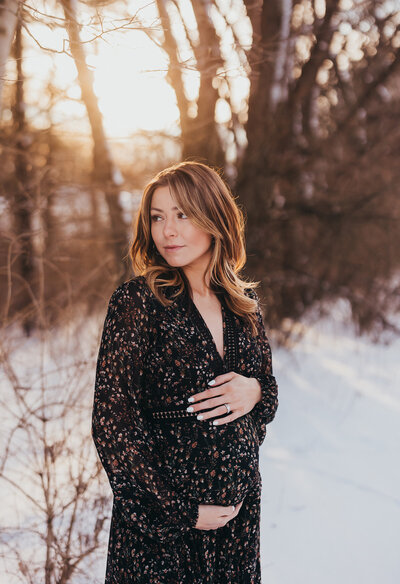 Maternity photo of mother holding stomach in a snowy forest