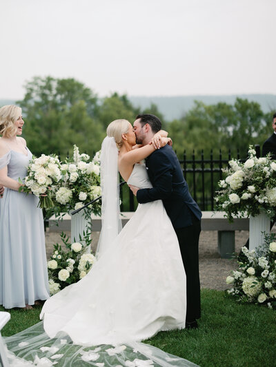Bride and groom kissing each other at the front of wedding ceremony and flower arrangements
