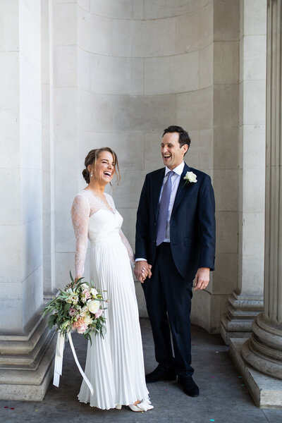 Bride and groom laughing in front of tall marble arch