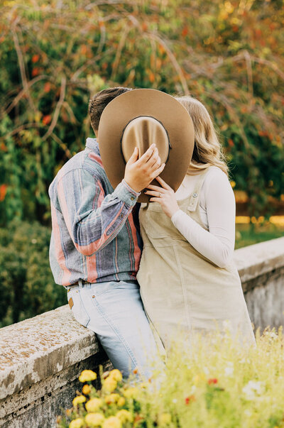 Couple kissing behind cowboy had leaning on a bridge