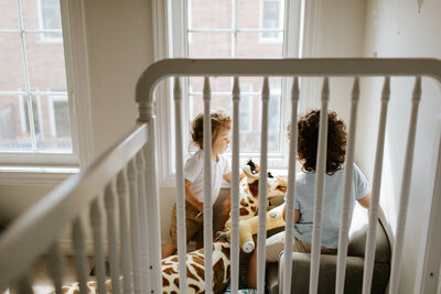 Two children sit in a sunlit room with large windows, joyfully playing with stuffed animals, including a giraffe—captured beautifully by a family photographer in Toronto.