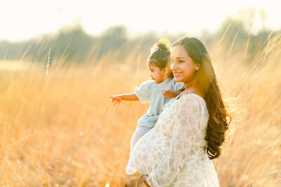 Pregnant mother holding her toddler daughter in a field of yellow grass