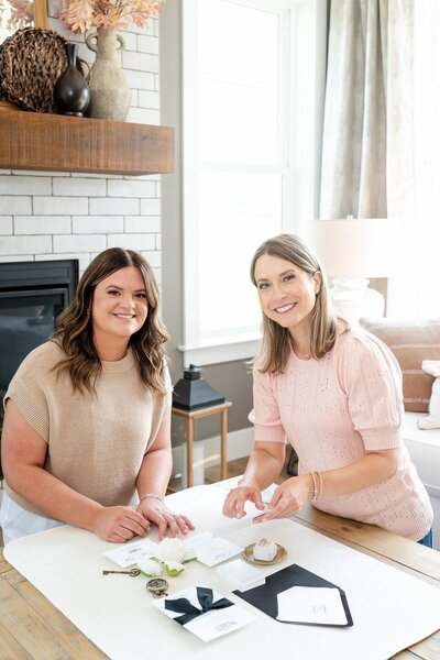 Two wedding stationers smiling and creating a flat lay
