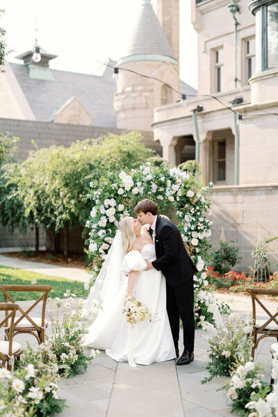 Bride and groom kissing in front of floral arch by chicago wedding planners