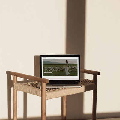 Chandler Randolph Showit website mockup on a computer. The computer is sitting on a neutral tan colored wooden stool.