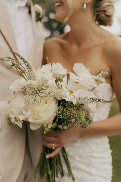 Bride smiles up at groom while she holds her green and white bridal bouquet