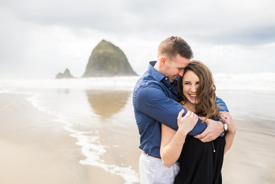 couple hugging close during a windy day at cannon beach