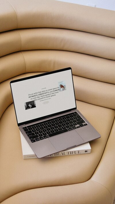Laptop and magazine sitting on tan modern couch. The laptop has a white website with text and photos