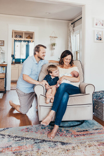 A sweet family looks at their newborn baby while they sit in a chair in their San Diego home