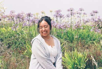 Creative Marketing Specialist Vanessa is here in the background is a field of flowers