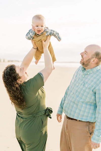 mother holds baby up to make him smile dressed in green and tans during family session by carrie pellerin