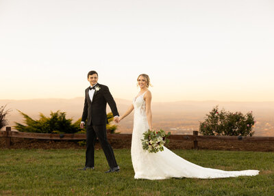 A groom holds the hand of his bride and leads her across the grass at Hidden Hill wedding venue.
