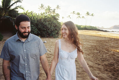 A couple hold hands and smile on the beach, representing Eugene wedding photographer Heathers commitment to celebrating love in all forms. 