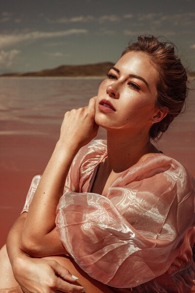 Women in pink dress, Puffy sleeves, touching her face, water in the background, blue sky