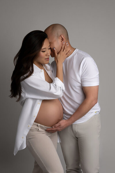 Intimate Austin maternity photography session capturing expectant couple in coordinated white outfits with tender connection at Cedar Park studio