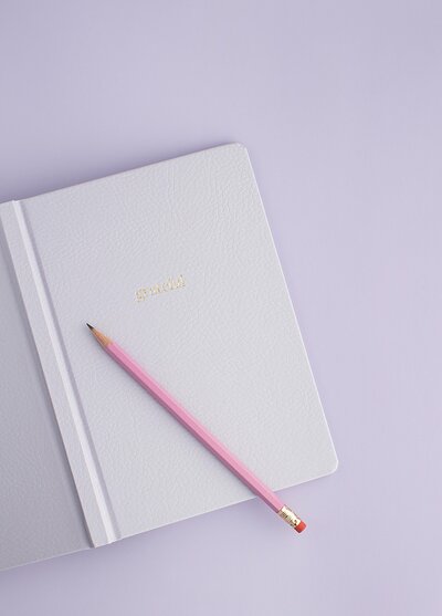Libreta abierta con lápiz sobre fondo morado.