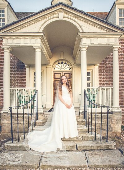 A bride in a white gown stands outside of a manor house in Reston Virginia