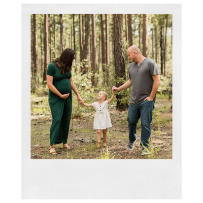 Polaroid photo of a family of three. The mom and dad are standing while holding their daughter's hands, who is standing between then in the Pine forest in Payson arizona