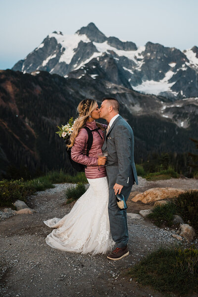 Bride in puffy coat kissing groom in front of Mount Skuksan at Artist Point!