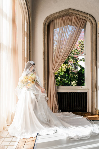 A bride with her veil covering her face and flowers, showing off her dress at Callanwolde Fine Arts Center. 
