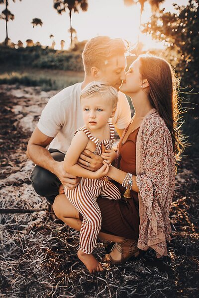 Mom and dad kissing while holding little boy in Tampa Florida family session. 