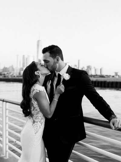 Bride and groom in a romantic kiss with the skyline of New York City in the background.