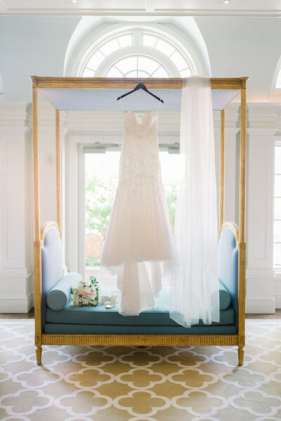 A white wedding dress hangs from a tall daybed with a long veil