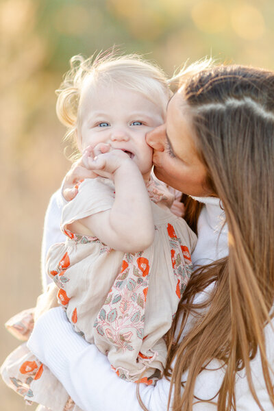 Mother holding her baby girl, planting a kiss on her cheek.