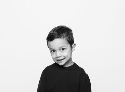 Young boy in a black and white portrait with a shy smile