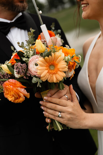 Close-up of the bride and groom holding their wedding flowers, capturing the delicate blooms and the couple's hands intertwined in a tender moment.
