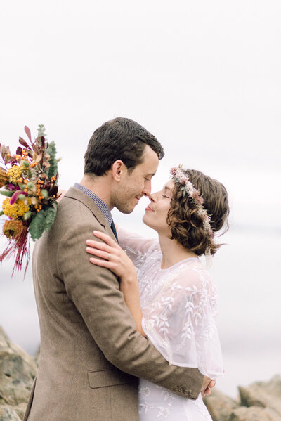 Cinematic wide shot of the couple embracing on the summit, with soft focus and natural light.
