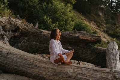 Woman meditating on a log by the water