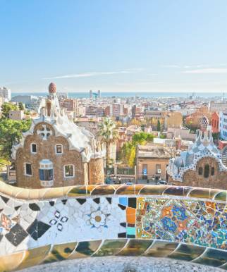 View of Barcelona skyline from Park Güell with Gaudí’s iconic colorful mosaic architecture in the foreground.