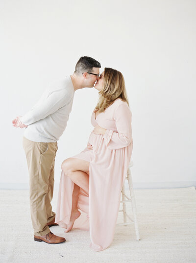pregnant mother in a blush pink dress kissing her husband by photographer in madison wi Talia Laird Photography