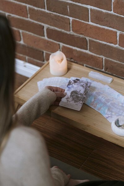Woman holding up a tarot card, with a deck of cards and a lit candle on the table.