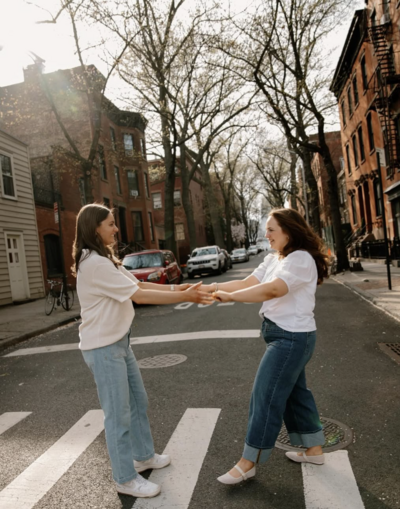 LGBTQ+ couple spinning and smiling together on city streets during their engagement photoshoot in New York City