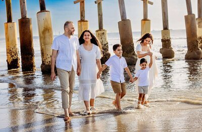 A family walks together on Cocoa Beach, with a beautiful pier visible in the distance.
