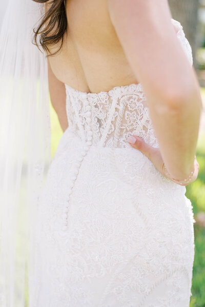 detail shot of the back of a brides dress as she stands with her hand on her hip