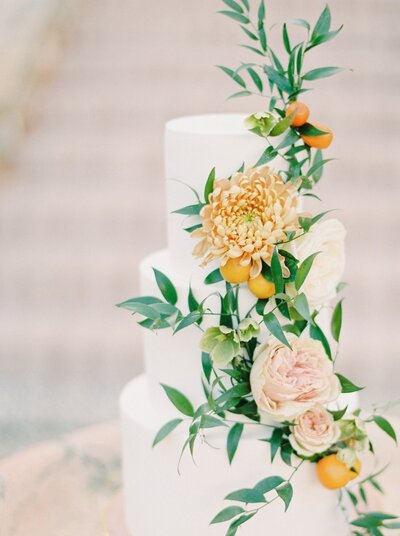 Bespoke wedding cake in white with orange flowers and greenery designed by ECLAT Destination Weddings Vienna
