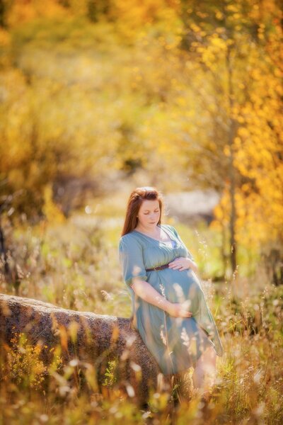 Maternity pictures of a mom wearing blue with a yellow flower in evening light.