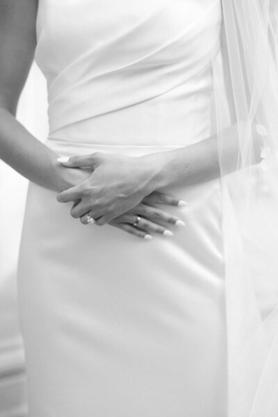 Close-up of a bride’s hands folded over her wedding dress.