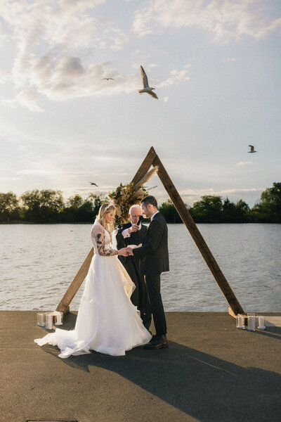 wedding couple saying their vows by the water as seagulls fly overhead at ubc boathouse