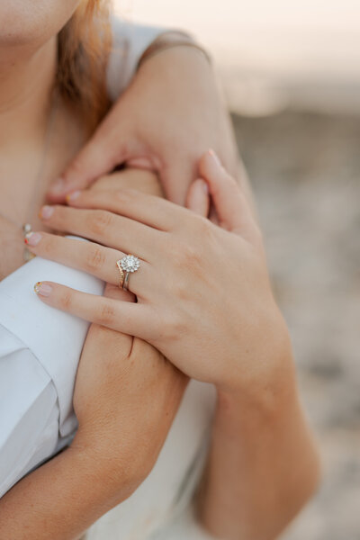 Engagement ring and wedding band on couple holding hands at sunset