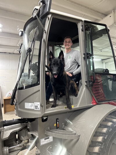 Man smiling from the driver's seat of a work vehicle with his black dog