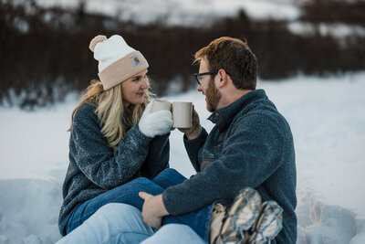 Engaged couple cuddle during snowy mountain engagement photos.