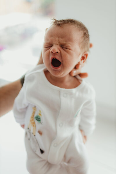 newborn abby wearing white yawning