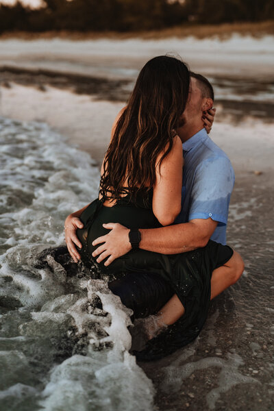 man and woman sitting in ocean kissing